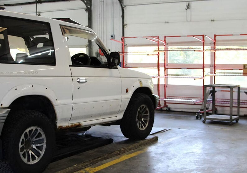 White SUV in a garage on a lift A white SUV parked on a lift in a garage. The vehicle is positioned for maintenance or repair.